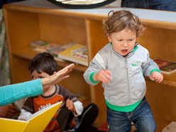 Young boy beating his arms in frustration with an adult supporting him from behind.