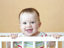 baby inside a crib holding on to the side and smiling