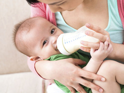 A baby being held by a woman and drinking from a bottle