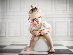 smiling toddler wearing glasses and sitting on a potty