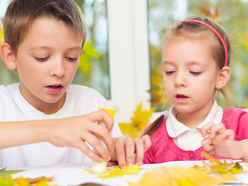 Boy and girl sticking leaves onto paper
