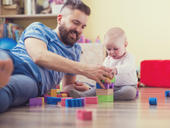 A baby and dad sit on the floor and play with blocks