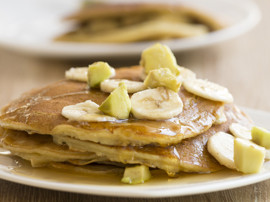 pancakes topped with slices of banana and chunks of apple, drizzled with syrup