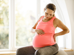 woman in early labour sitting on a birth ball and rubbing her back and belly