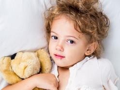 Little girl with cold sore lying in bed cuddling teddy bear
