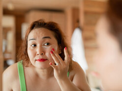 woman putting on face cream while looking at herself in a mirror