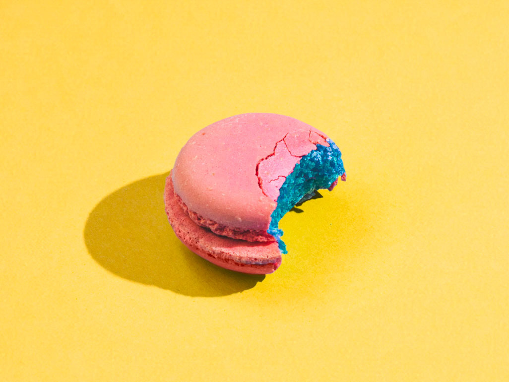 A pink macaroon with a bite out of it, revealing a blue interior