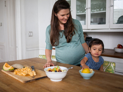 Toddler picking up an orange while a pregnant woman watches