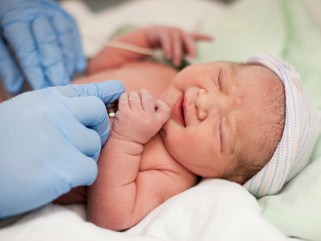 doctor wearing medical gloves holding a newborn baby with