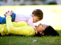 Mom lying on the grass with her toddler lying on her belly