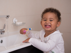 Child smiling into the camera while brushing teeth at the sink