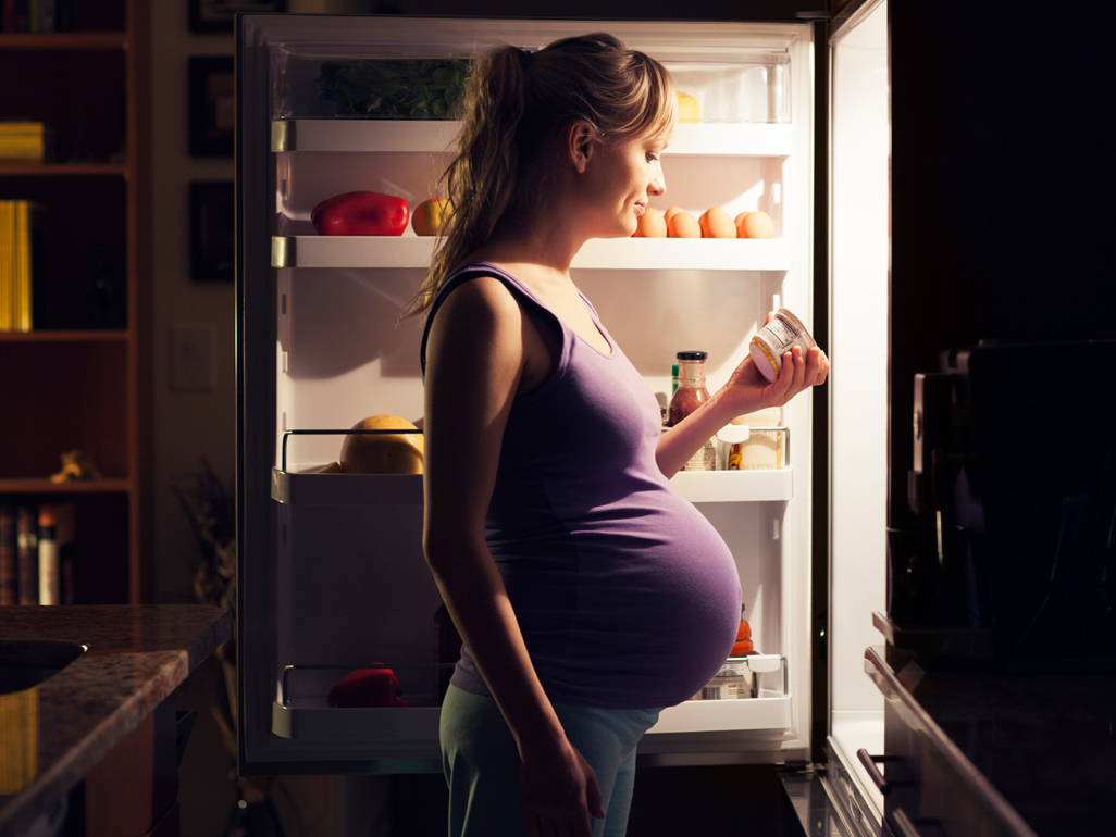 a pregnant woman standing in front of a refrigerator in the middle of the night 