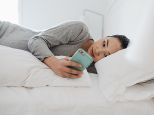 A woman lies on her side in bed and looks at her phone.