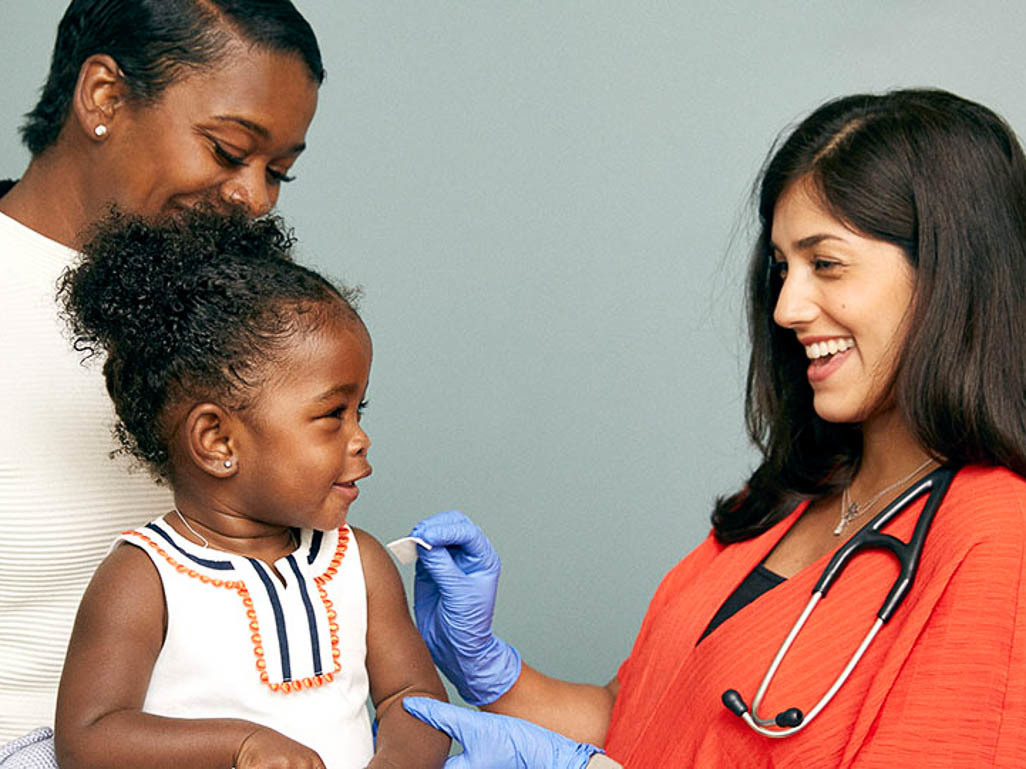 little girl sitting on an adults lap while medical professional prepares to give her a vaccination in her arm