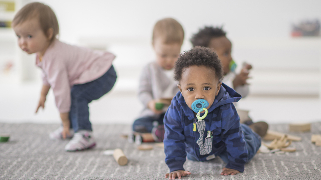 Four infants crawling and playing on the floor at daycare.