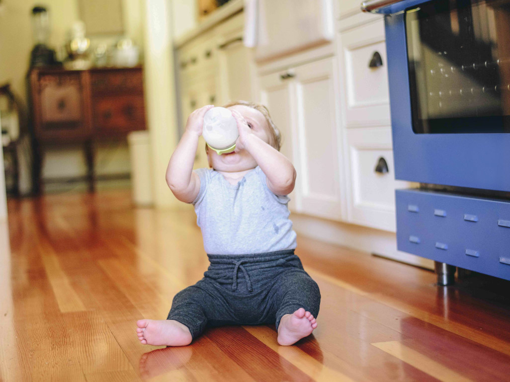 A baby drinks from a bottle while sitting in a living room