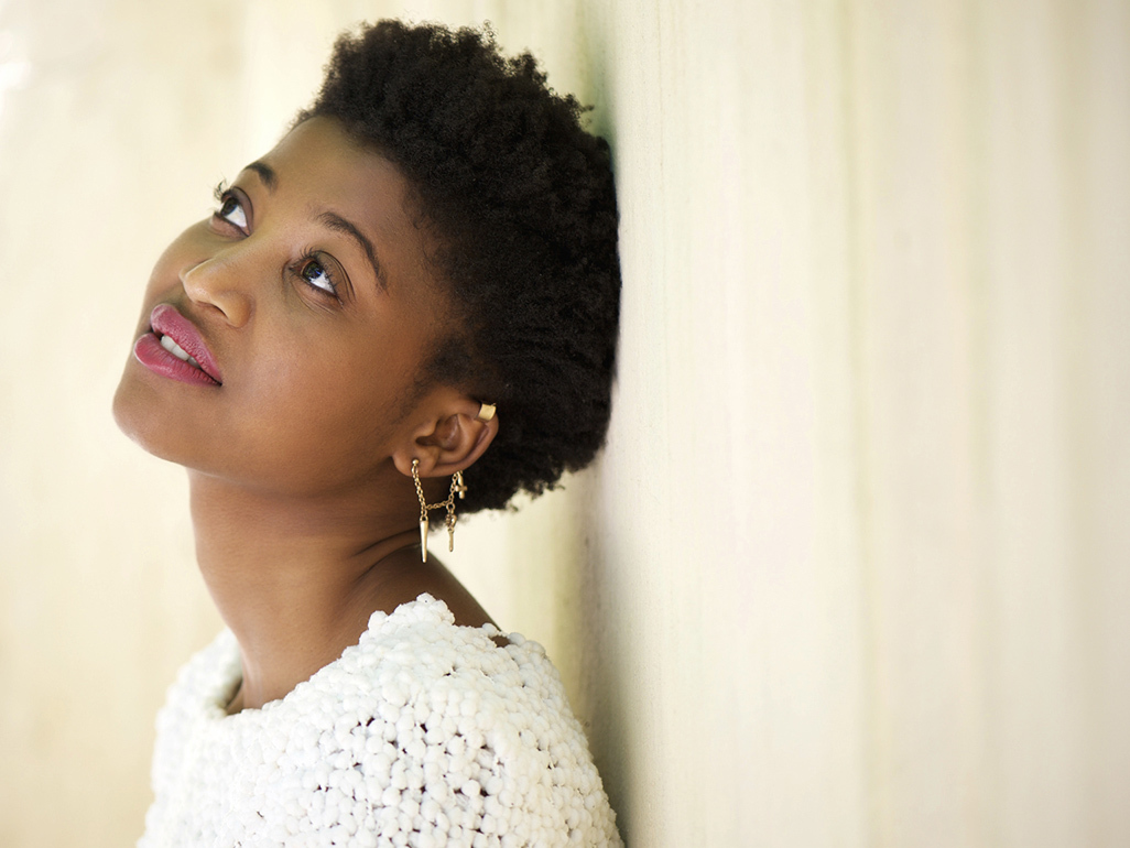 A woman with multiple ear piercings leaning up against a wall