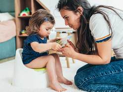 A mom reading a book with a toddler sitting on a training potty