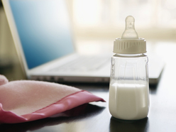 baby bottle with milk on a desk next to a laptop and a pink blanket