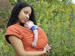 This image shows a beautiful young mom holding a baby in a sling. 