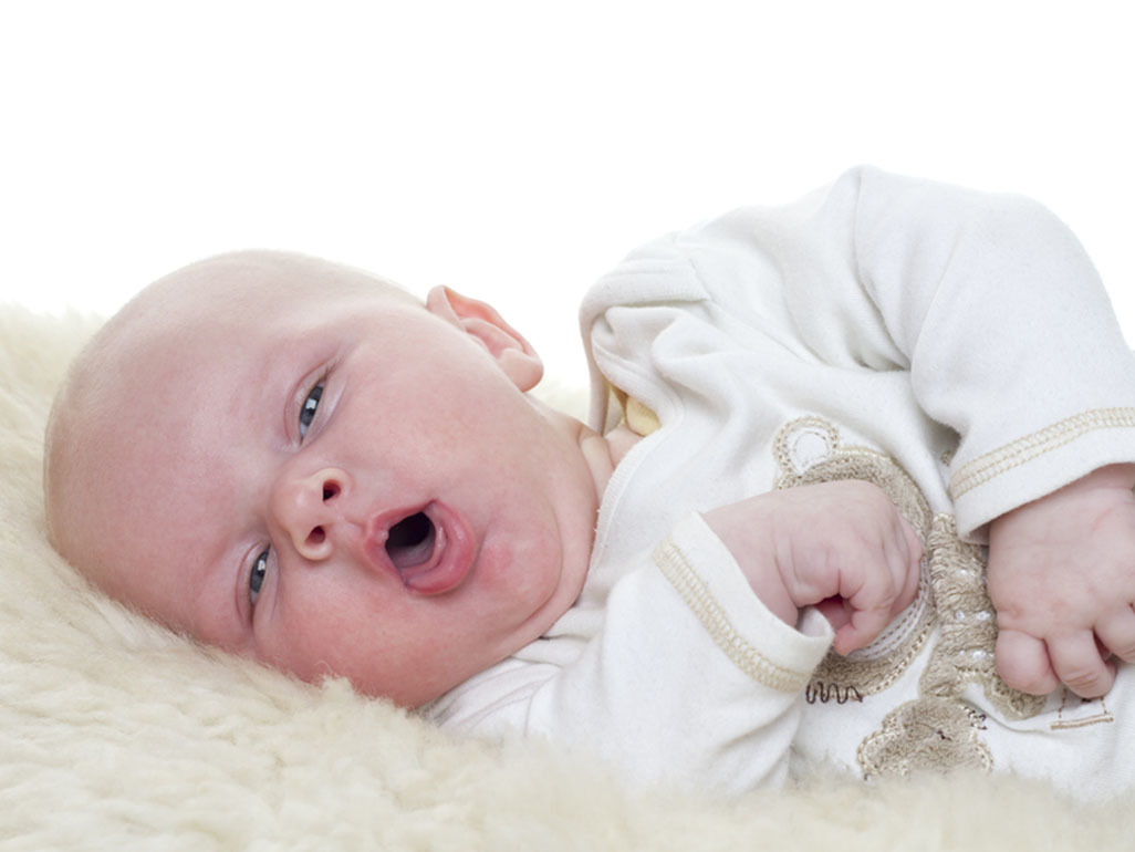 A baby lying on her side and making an 'o' shape with her mouth.