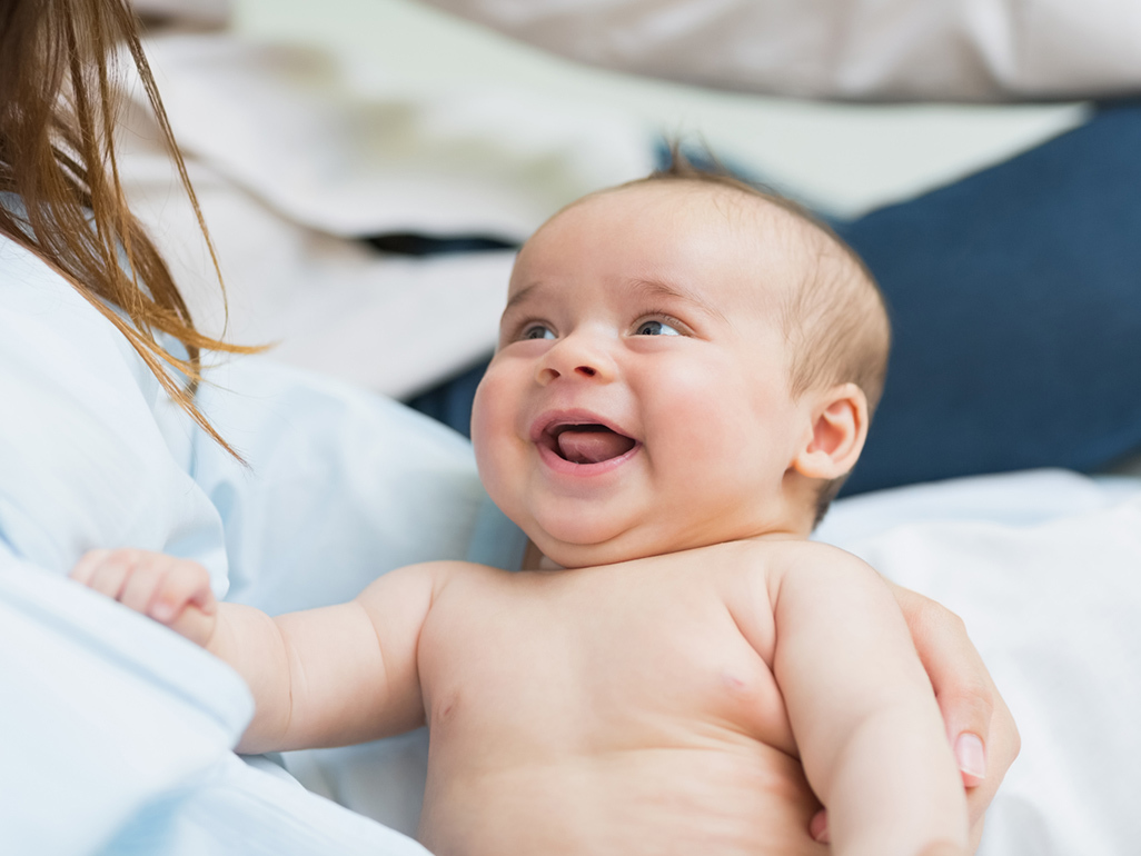 Mum holds baby as baby open mouth smiles up at mum