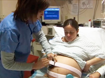 Nurse attaching two heartbeat monitors to pregnant woman's twin bump