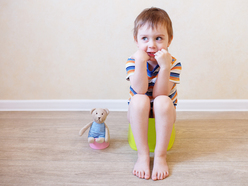 A toddler boy sitting on a potty training toilet, next to a stuffed bear on a mini toilet 