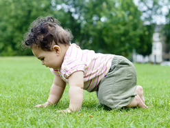 curly haired baby crawling in grass