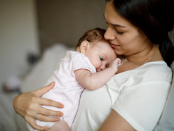 A postpartum mom cuddling her newborn baby.