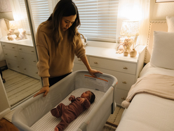 A tired mom looking at her baby in a bassinet