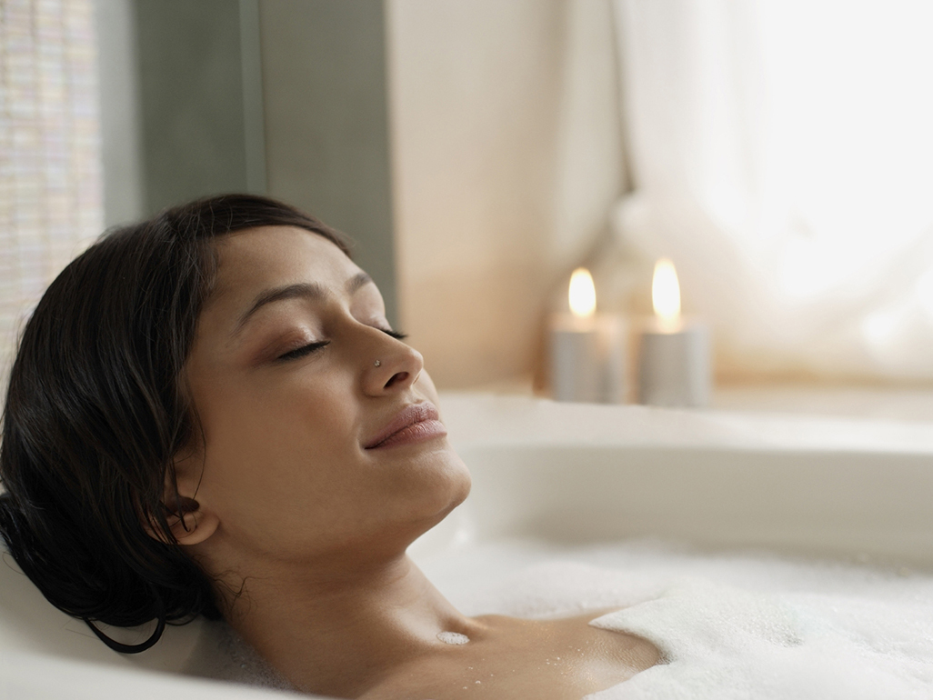 Woman relaxing in a bubble bath with candles