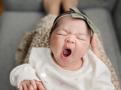 Yawning newborn being help up to the camera