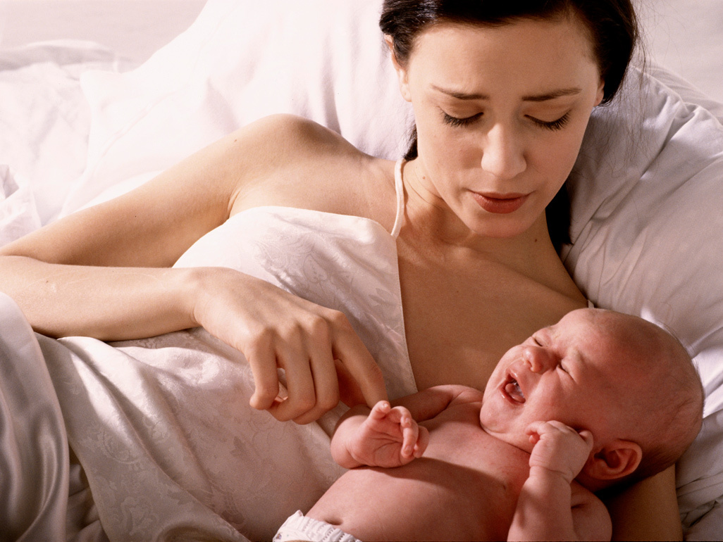 Bebê chorando na cama ao lado da mãe